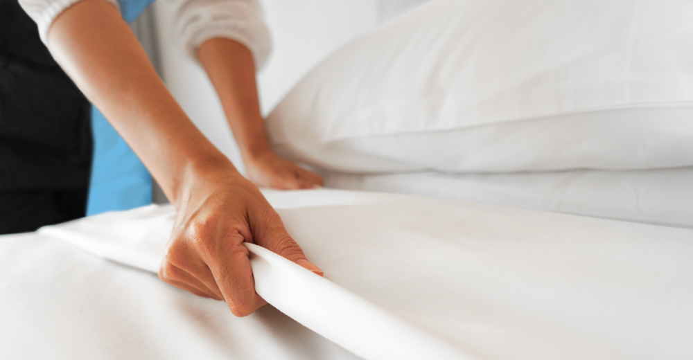 Femme de ménage qui tire les draps pour faire le lit.